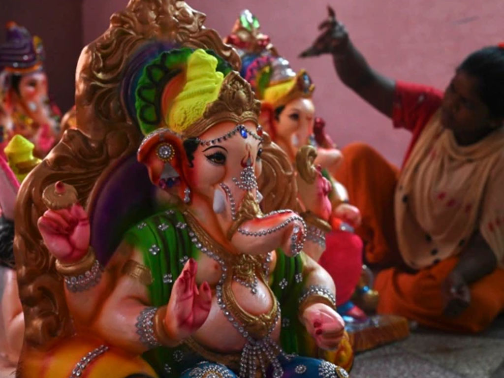 Seorang pengrajin mendekorasi patung dewa Hindu